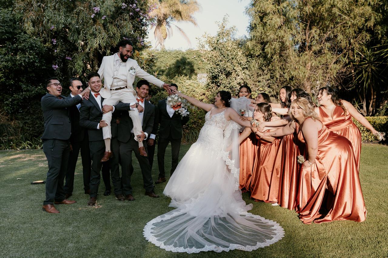 novio en brazos de sus best men en bodas mientras las damas de honor tiran del brazo de la novia que intenta alcanzar su mano