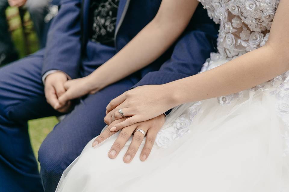 Pareja de novios agarrados de la mano mostrando anillos de boda