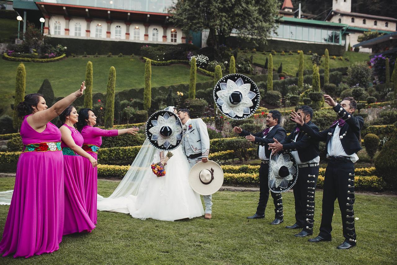 Damas y damos de honor se divierten tirando sombreros mariachi con novios besándose en el centro