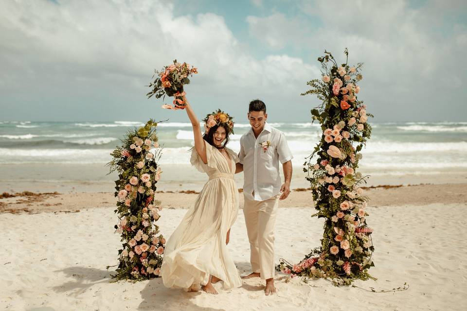 pareja de recién casados en playa con arco de flores