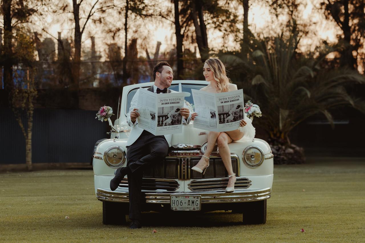 Videógrafo de bodas filmando a dos novios leyendo un periódicos sentados en un auto blanco