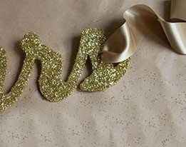 Una vez seca la brillantina, coloca el listón en los orificios para que puedas colgar el letrero. Pu