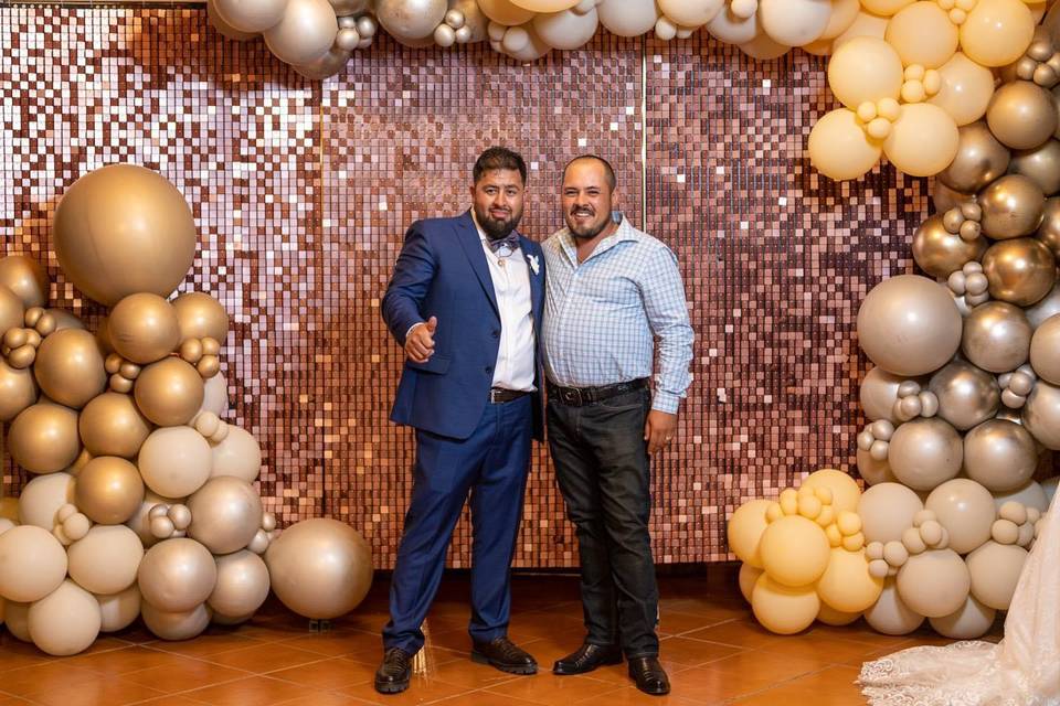 Novio con invitado en una pared decorada con globos dorados