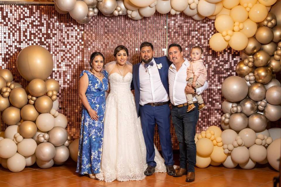 Novios posando con invitados en un spot lleno de globos dorados