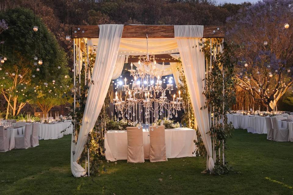 Montaje de mesa de novios con una carpa con luces y plantas