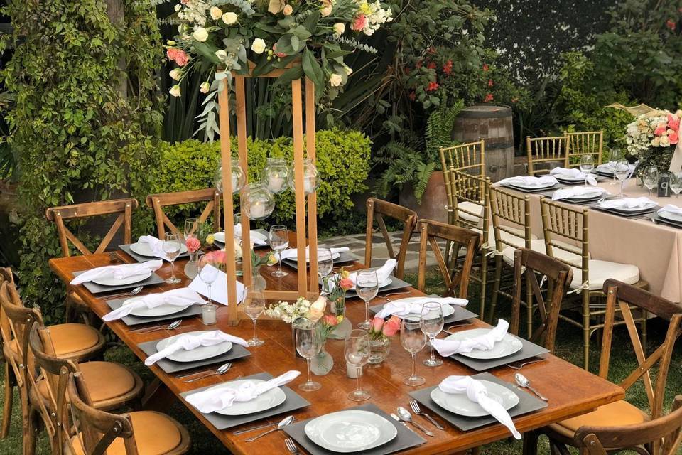 Mesa de madera con vajilla blanca y arreglos florales altos