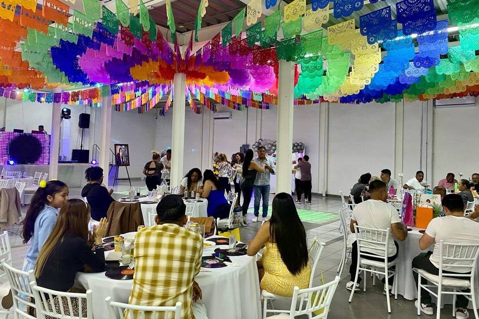 Invitados sentados en mesas y techo decorado con papel picado