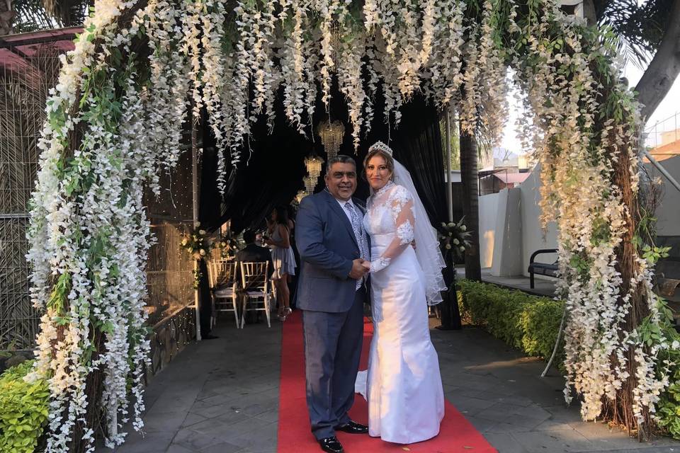 Posando sobre una alfombra roja y un arco de flores