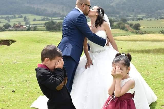 Novios besándose en un jardín y niños tapándose los ojos