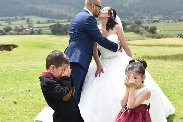 Novios besándose en un jardín y niños tapándose los ojos