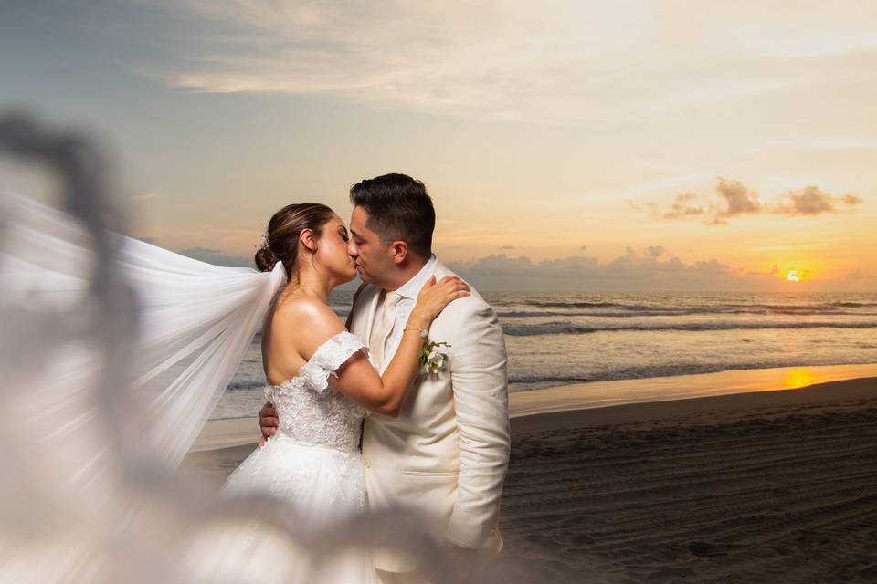 Novios dándose un beso en el atardecer de la playa