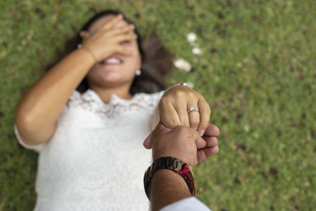 Novia acostada en el pasto tapándose los ojos con la mano y con la otra sosteniendo la mano del novio