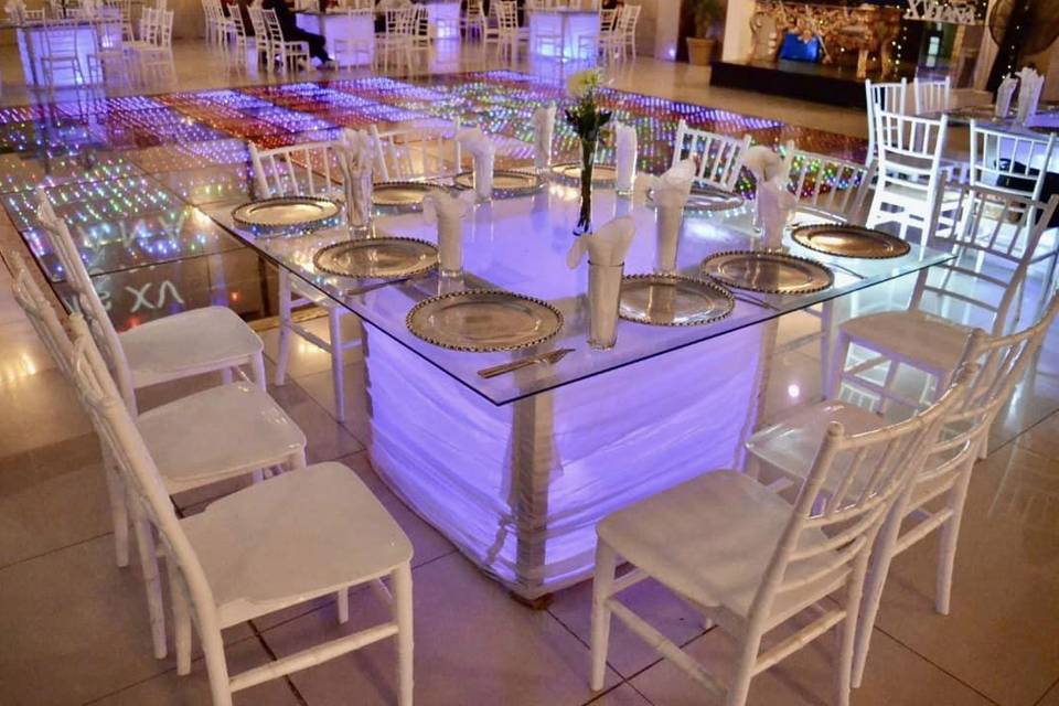 Mesa de cristal iluminada con sillas blancas y pista led