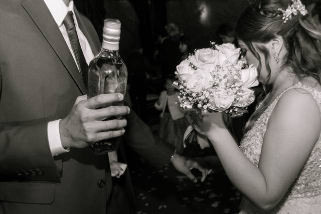 Novios sosteniendo un ramo y una botella