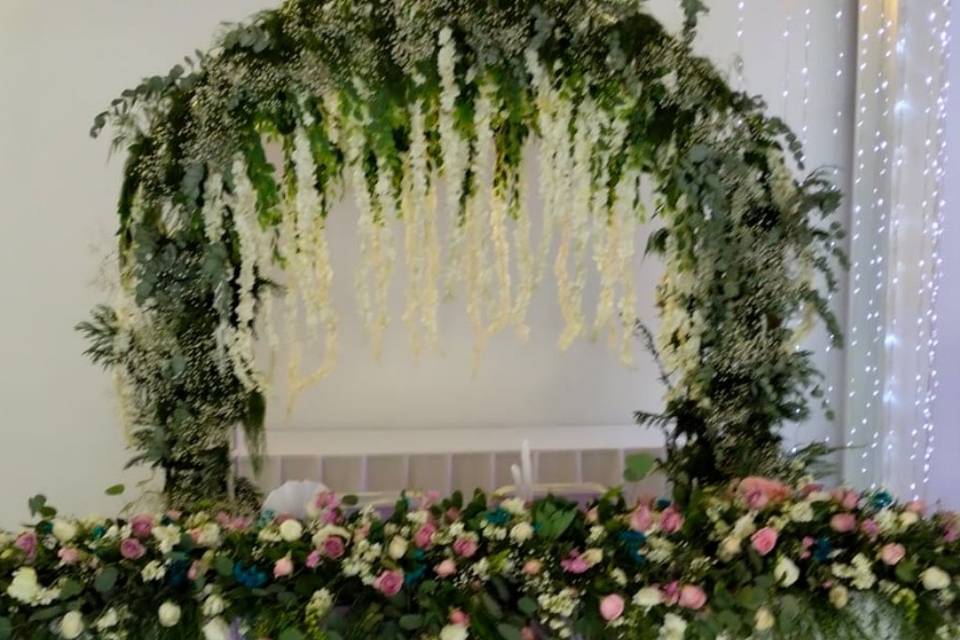 Mesa de novios decorada con flores y un arco detrás