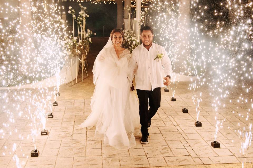 Novios agarrados de la mano caminando entre chisperos