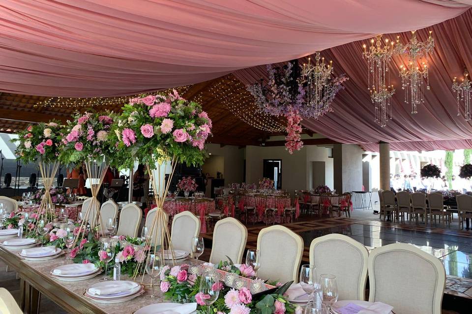 Espacio decorado con tela rosa, candelabros, centros de mesa con flores