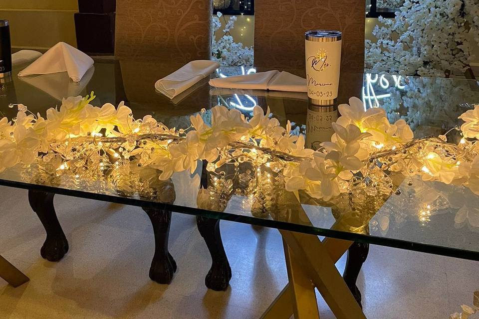Mesa de novios con arco de flores blancas y letrero neón