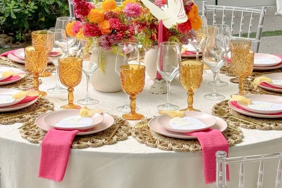 Mesa redonda con copas amarillas, flores en el centro y platos blancos