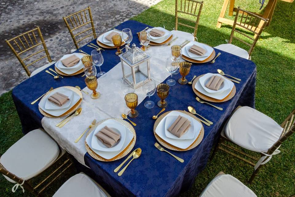 Mesa cuadrada con cubiertos dorados y mantel azul