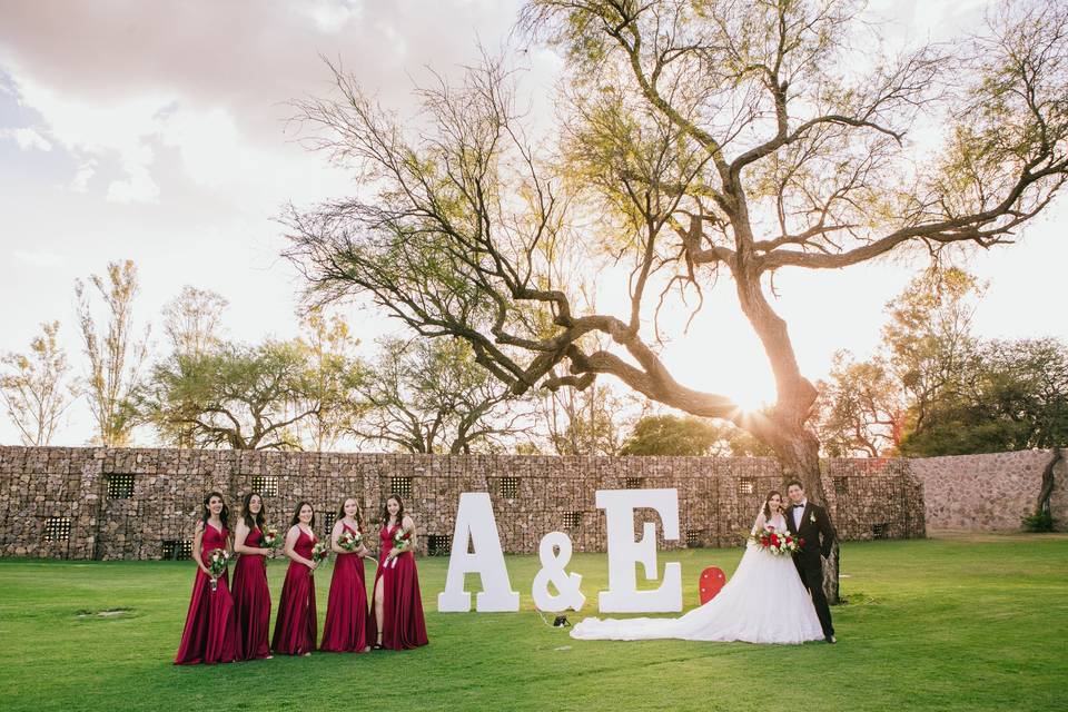 Pareja posando junto a las damas de honor en un jardín con letras gigantes blancas