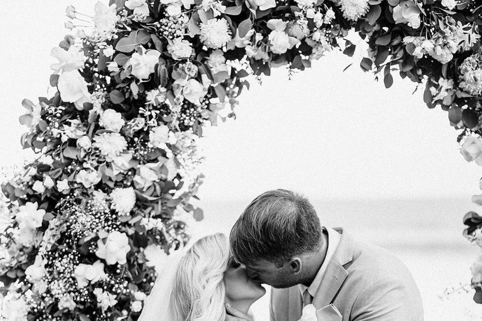 Novios besándose frente a un arco de flores