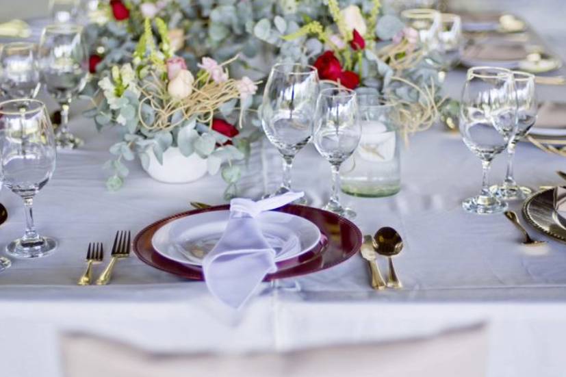 Mesa con platos y cubiertos dorados, servilletas blancas y arreglo floral