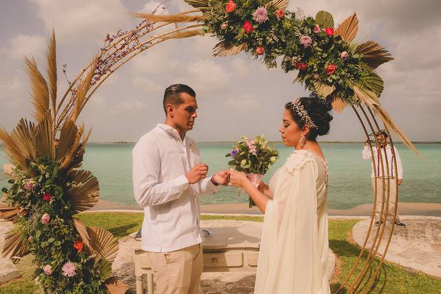 Novio poniéndole el anillo a la novia frente a un arco de flores