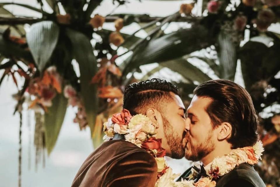 Novios besándose con collares de flores en su cuello