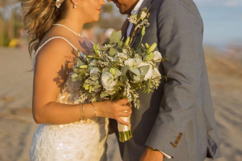 Recién casados en la playa y novia sosteniendo su ramo
