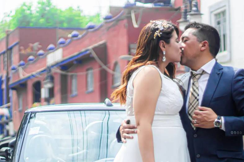 Novios dándose un beso frente a un auto blanco