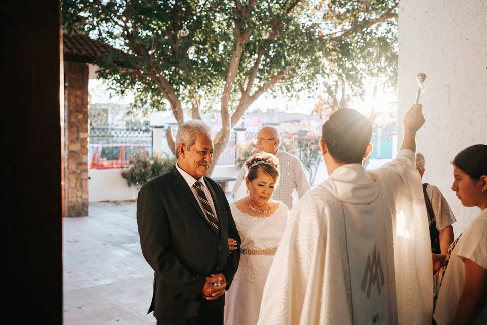 Novia con sus padre en la entrada de la iglesia frente al sacerdote