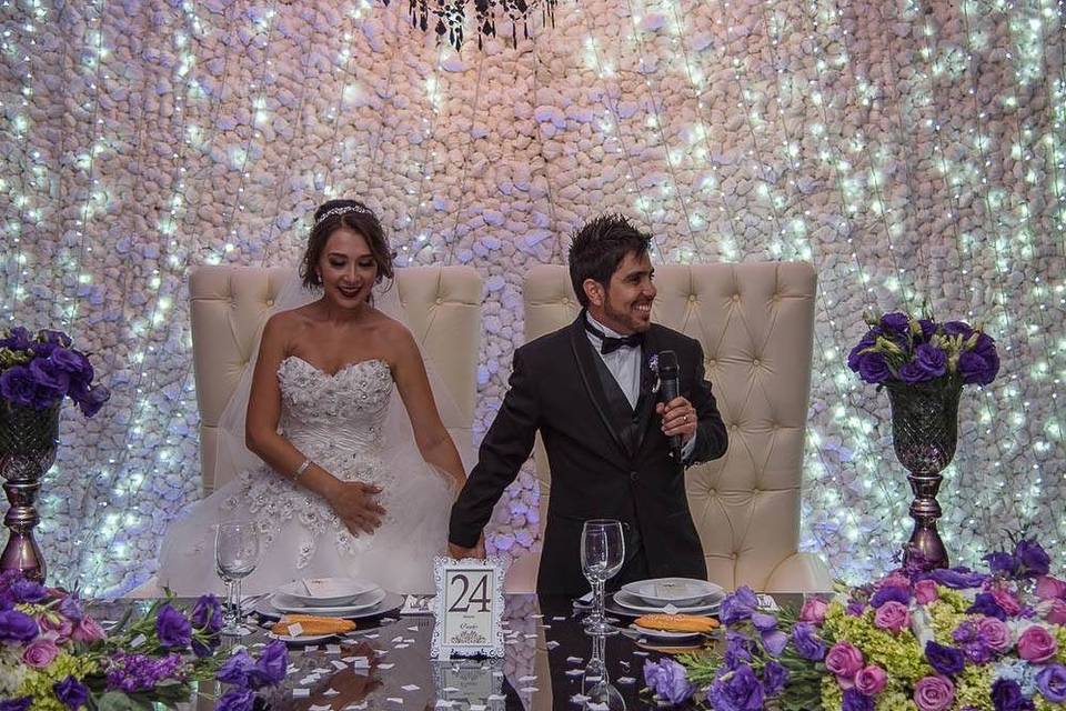 Pareja en su mesa de novios decorada conr osas rosas y moradas