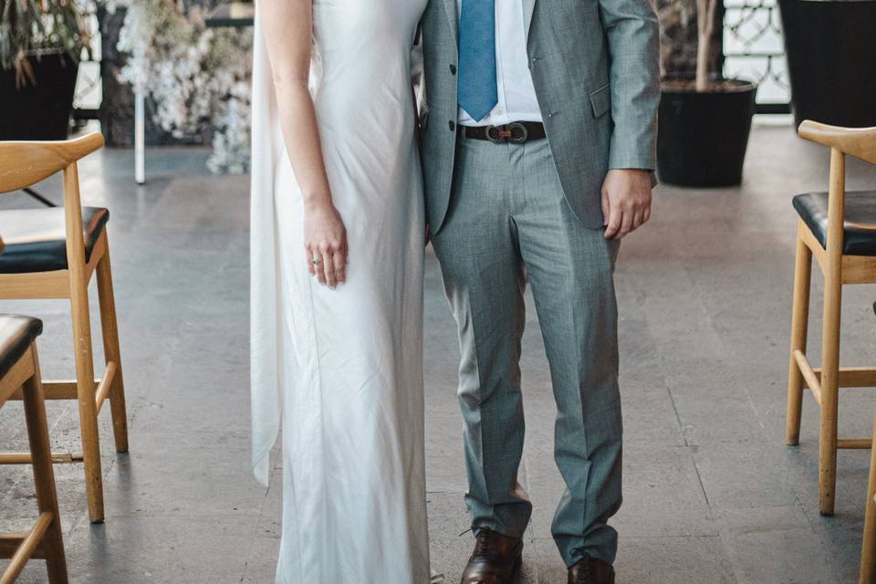 Novios posando en un salón frente a un arco de flores blancas