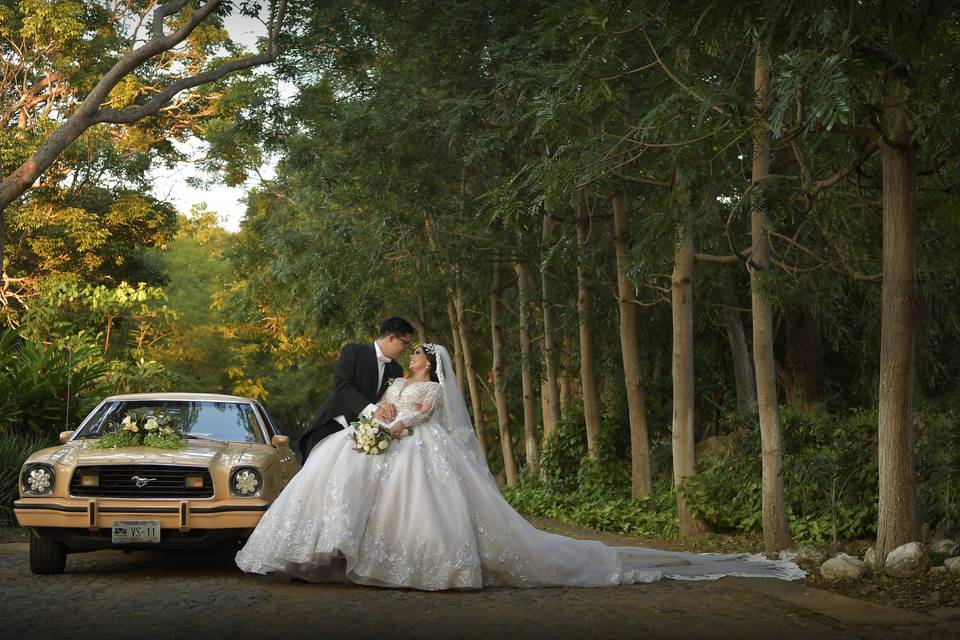 Novios posando a lado de un auto clásico