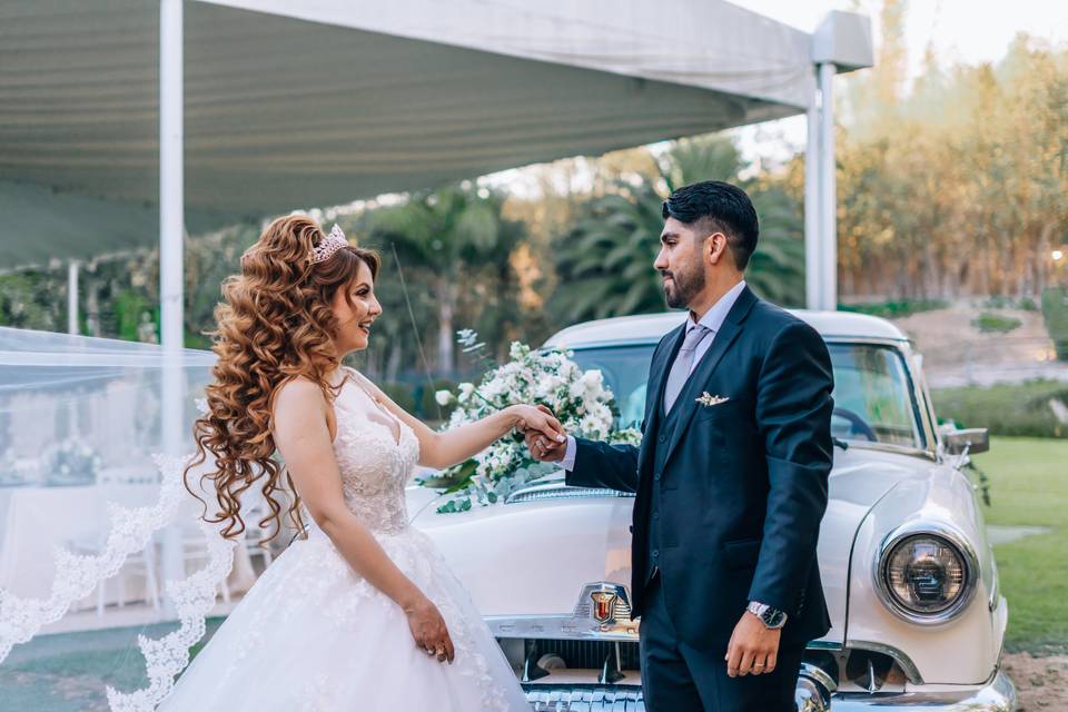 Novios dándose la mano frente a un auto clásico