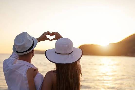 Pareja viendo el atardecer y haciendo un corazón con las manos