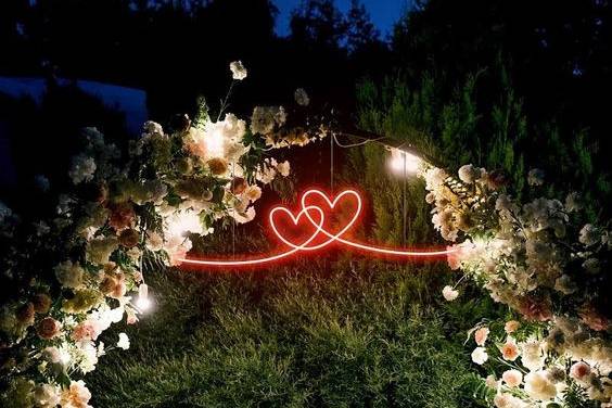 Corazones en neón rojo en un arco de flores