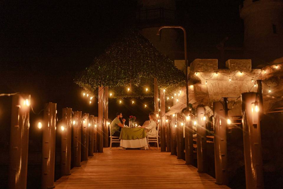 Puente de madera con luces y mesa con una pareja cenando