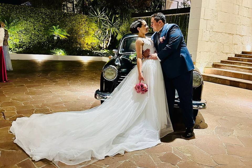 Novios posando frente a un auto clásico