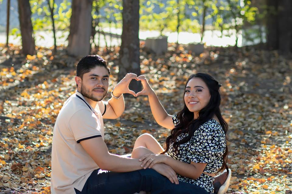 Novios sentados en el bosque haciendo un corazón con la mano