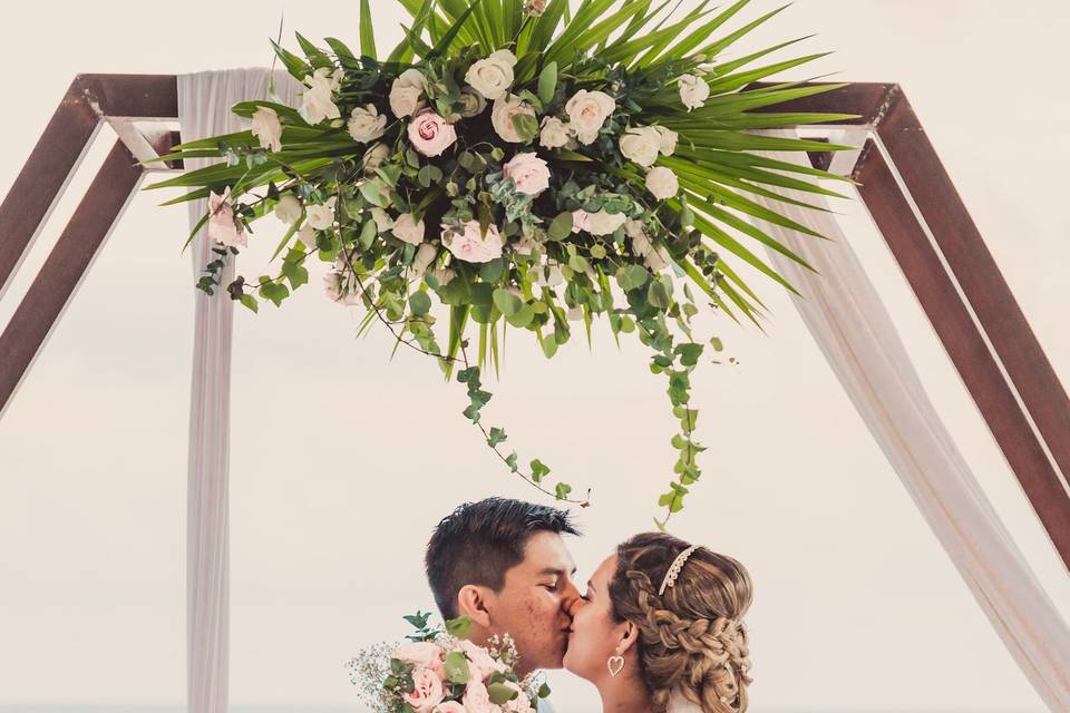 Novios besándose frente a una estructura de flores