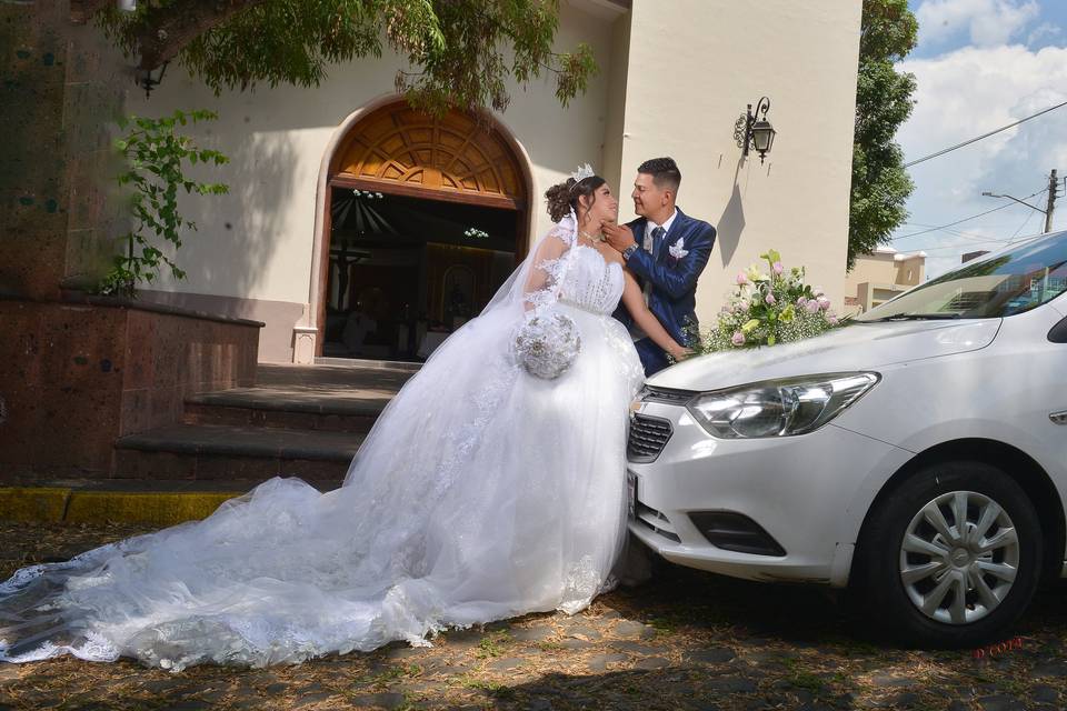 Novios posando frente a la iglesia y el carro