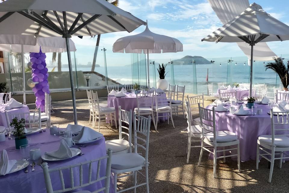 Terraza con montaje de mesas blancas con manteles lilas