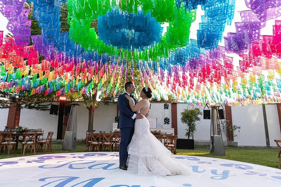 Novios bailando en la pista con papel picado de colores en el techo