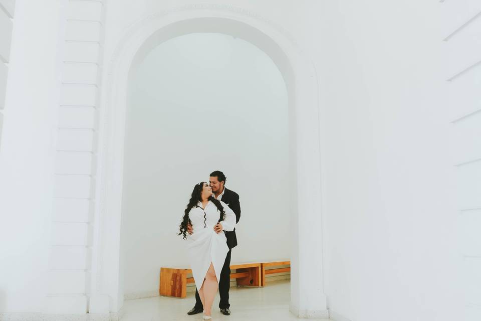 Novios posando bajo un arco blanco