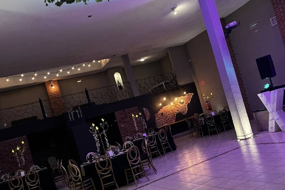 Salón con mesas redondas negras y sillas doradas