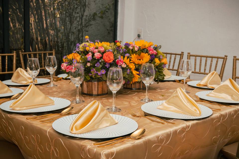 Mesa con mantel y servilletas doradas y arreglo con flores de colores