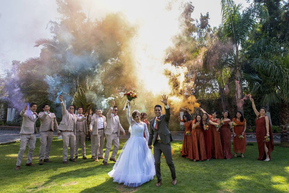 Novios en el jardín con sus damas de honor y bestmen con humo de colores