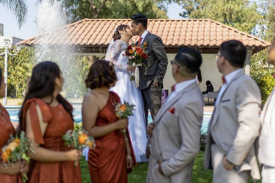 Novios besándose frente a las damas de honor y bestmen